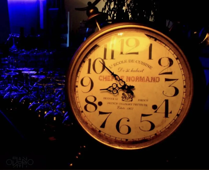 Une horloge ancienne éclairée, posée devant une rangée de verres bleutés.